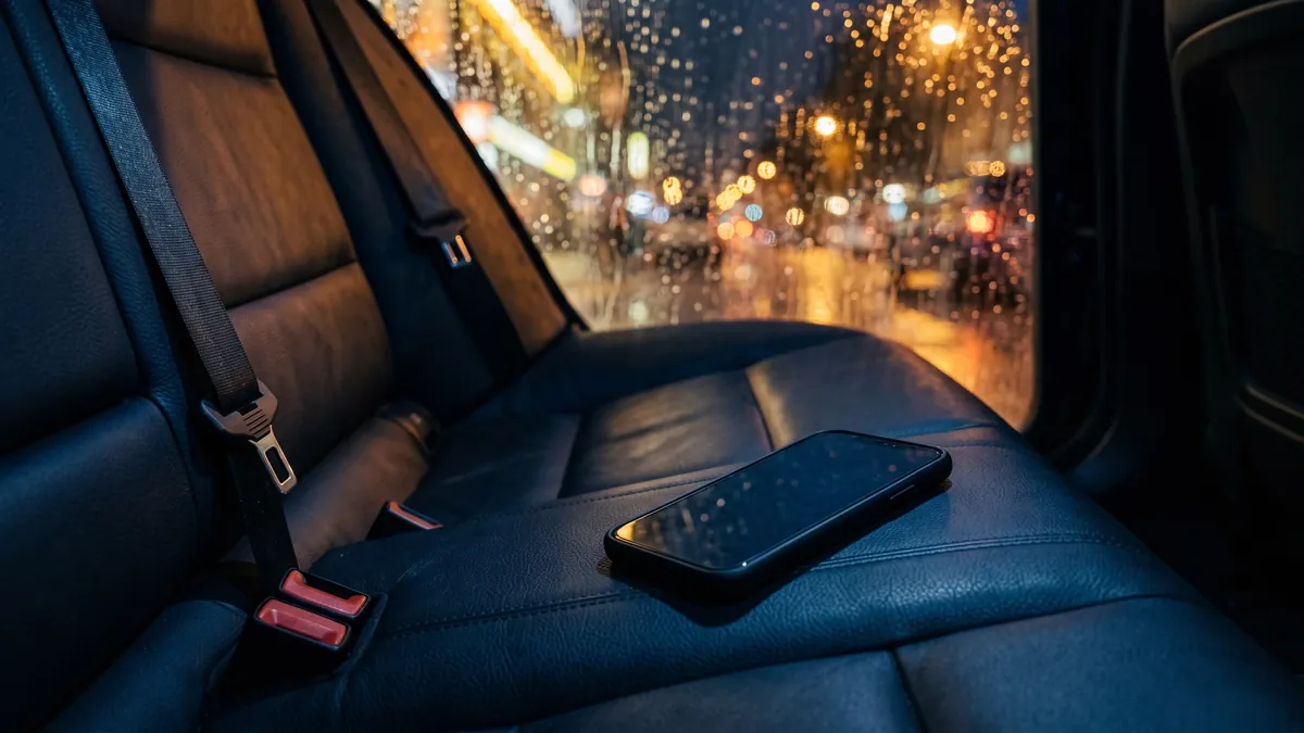 El asiento trasero vacío de un auto de noche, un teléfono en el asiento y lluvia en la ventana.